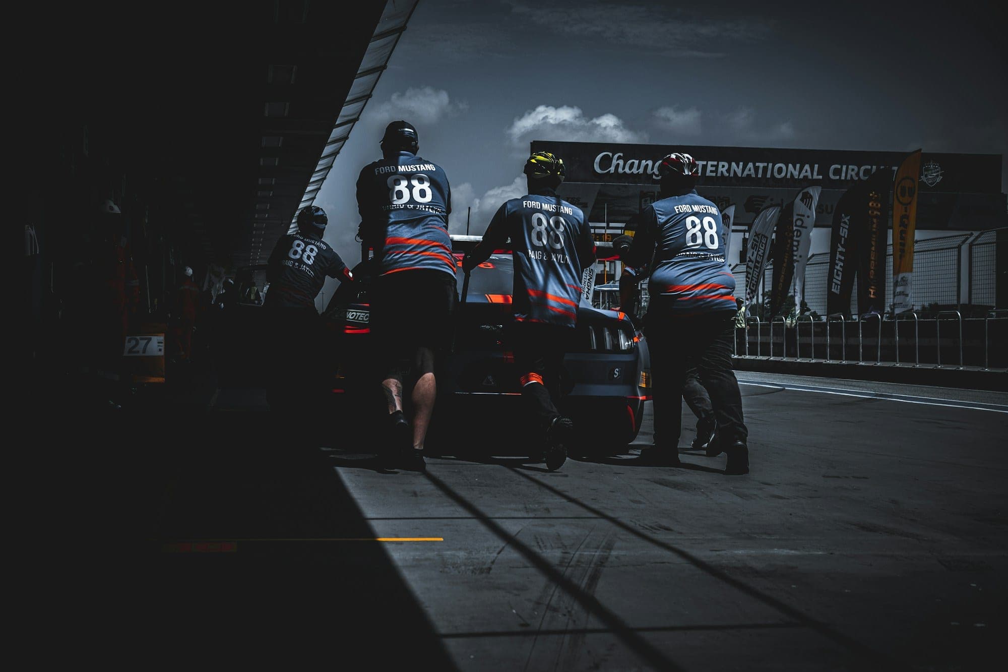 Crew members pushing a GT4 race car along the pit lane, reference photography
